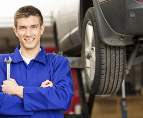 Portrait of a happy young car mechanic holding wrench with car on hoist in background. Horizontal shot.